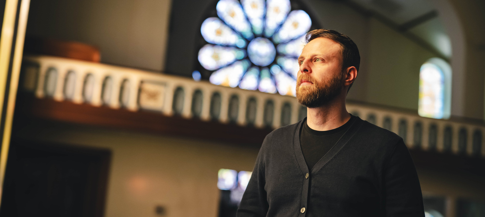 Dean Caivano looks stoically off into the distance standing in a church converted into a church.