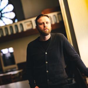 Dean Caivano poses for a photo in a church converted into a classroom wearing a dark blue sweater.